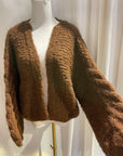 a white mannequin with a brown hand knit sweater hanging on it with a white background