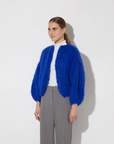 Person wearing a blue knitted cardigan over a white shirt on a light gray background