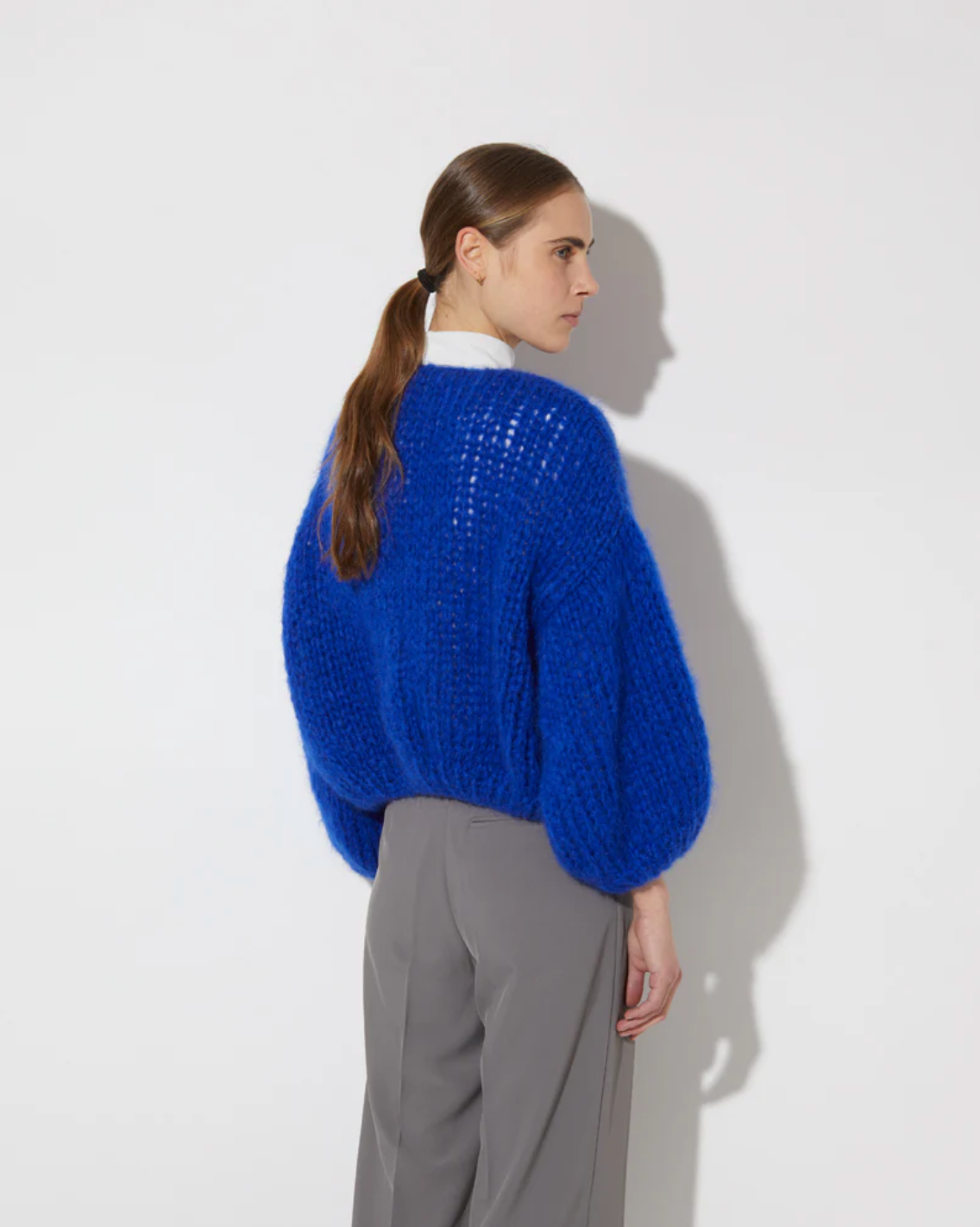 Person wearing a blue sweater and gray pants against a white background