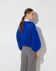 Person wearing a blue sweater and gray pants against a white background