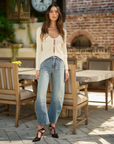 Woman standing outdoors in a casual setting with wooden chairs and tables.