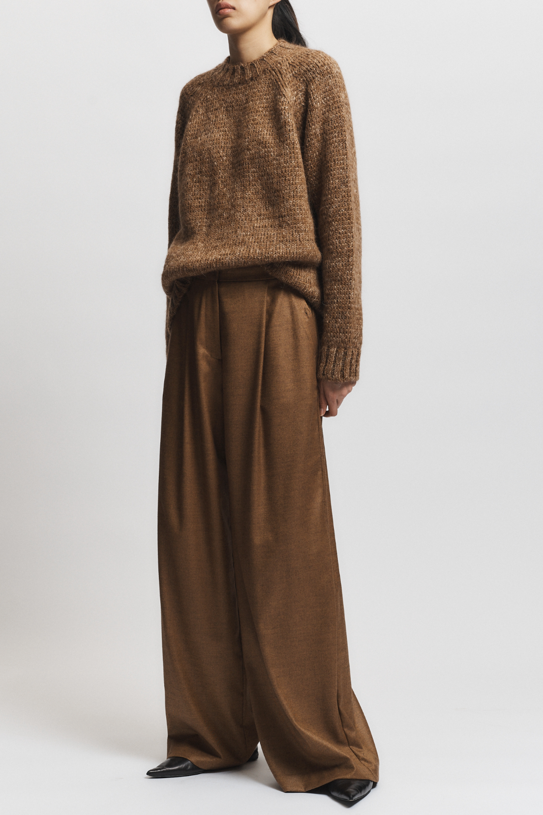 Person wearing a brown knitted sweater and wide-leg pants on a white background