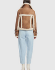 Person wearing a brown shearling jacket with white trim on a white background