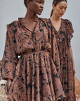 Two women wearing patterned dresses standing against a neutral background