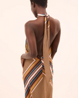 Woman wearing a patterned dress with a long scarf over her shoulder on a beige background