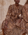 Woman wearing a patterned dress sitting against a neutral background