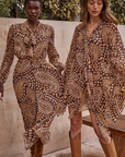 Two women wearing patterned outfits sitting on a stone bench outdoors.
