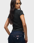 Woman wearing a black t-shirt and dark blue jeans on a light gray background
