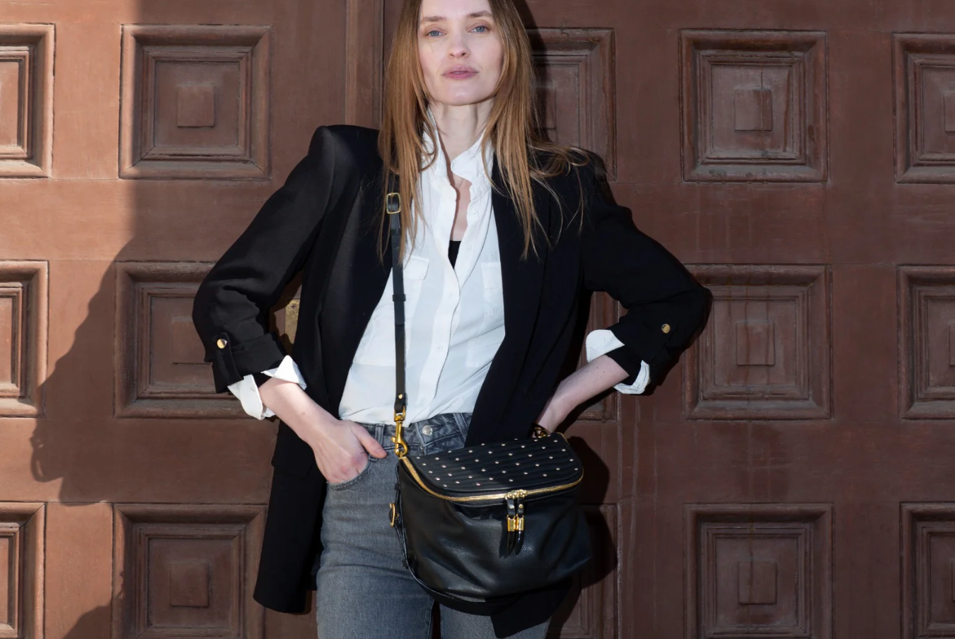 Woman holding a black studded handbag against a wooden door background