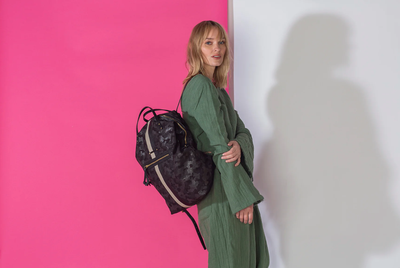 Woman holding a black backpack against a pink and white background
