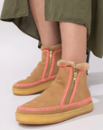 Tan winter boots with pink zippers worn by a person in an olive green skirt.
