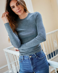 Woman wearing a gray sweater and blue jeans indoors.