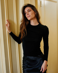 Woman in a black outfit standing against a beige wall.