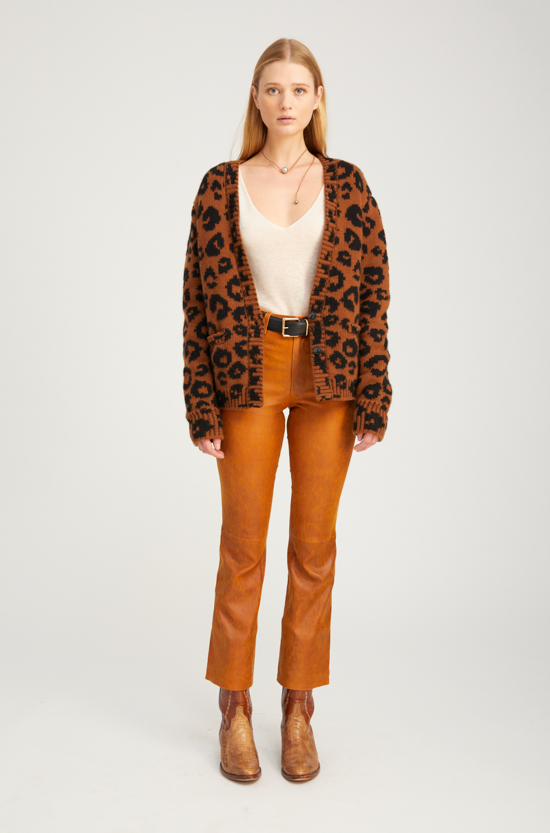 Woman wearing a leopard print cardigan, white top, brown pants, and brown boots on a white background