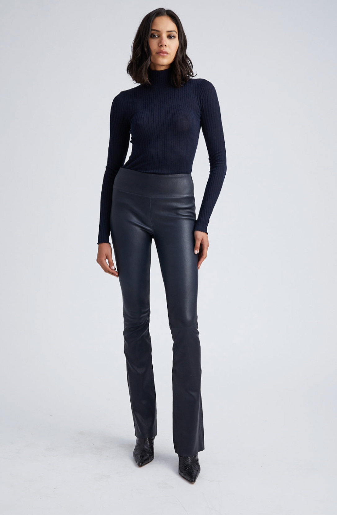 Woman wearing a black turtleneck and leather pants on a white background