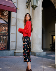 Woman in a red sweater and patterned pants standing in an urban setting.