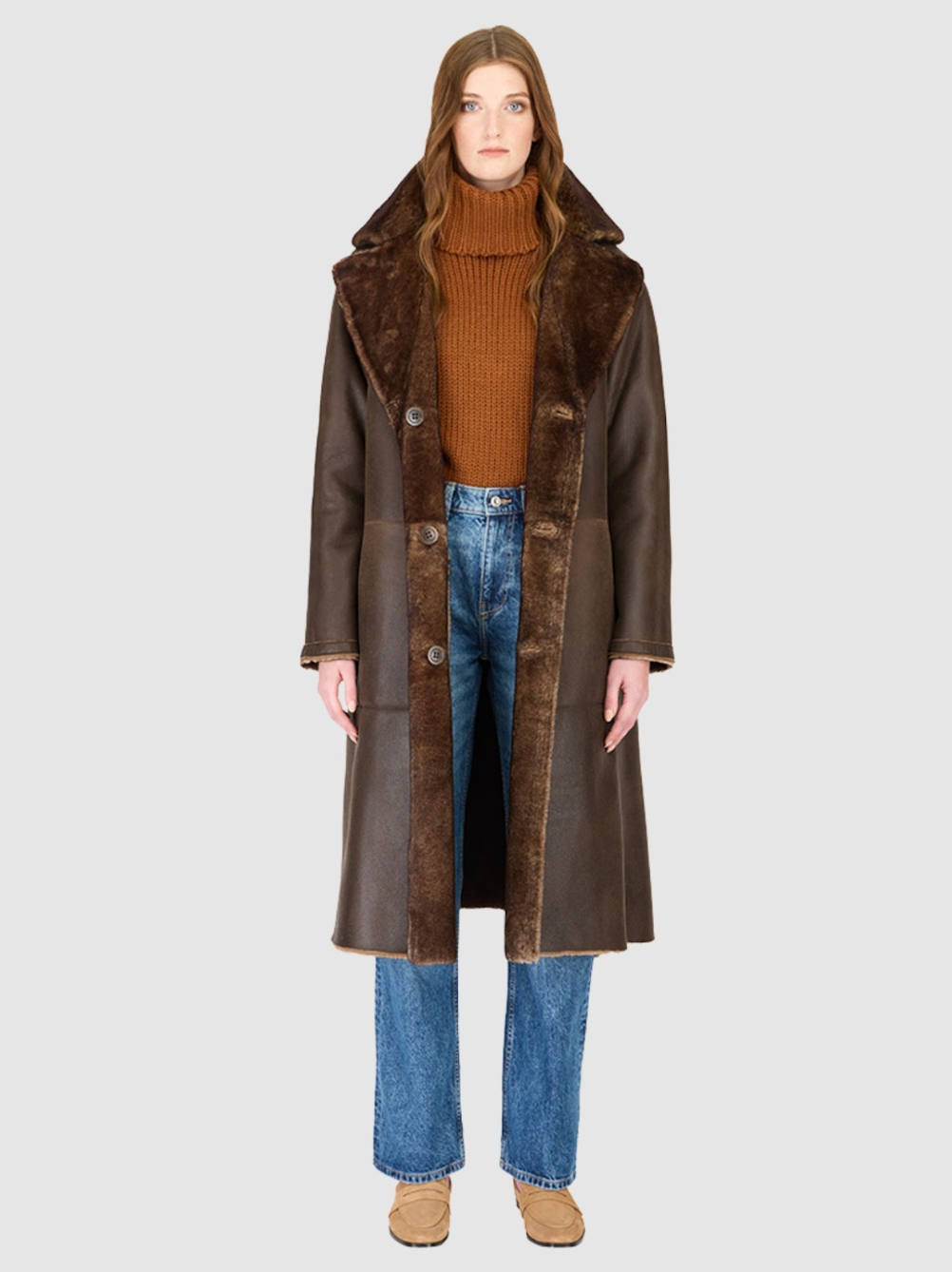 Person wearing a brown shearling coat with fur collar on a white background