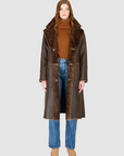 Person wearing a brown shearling coat with fur collar on a white background