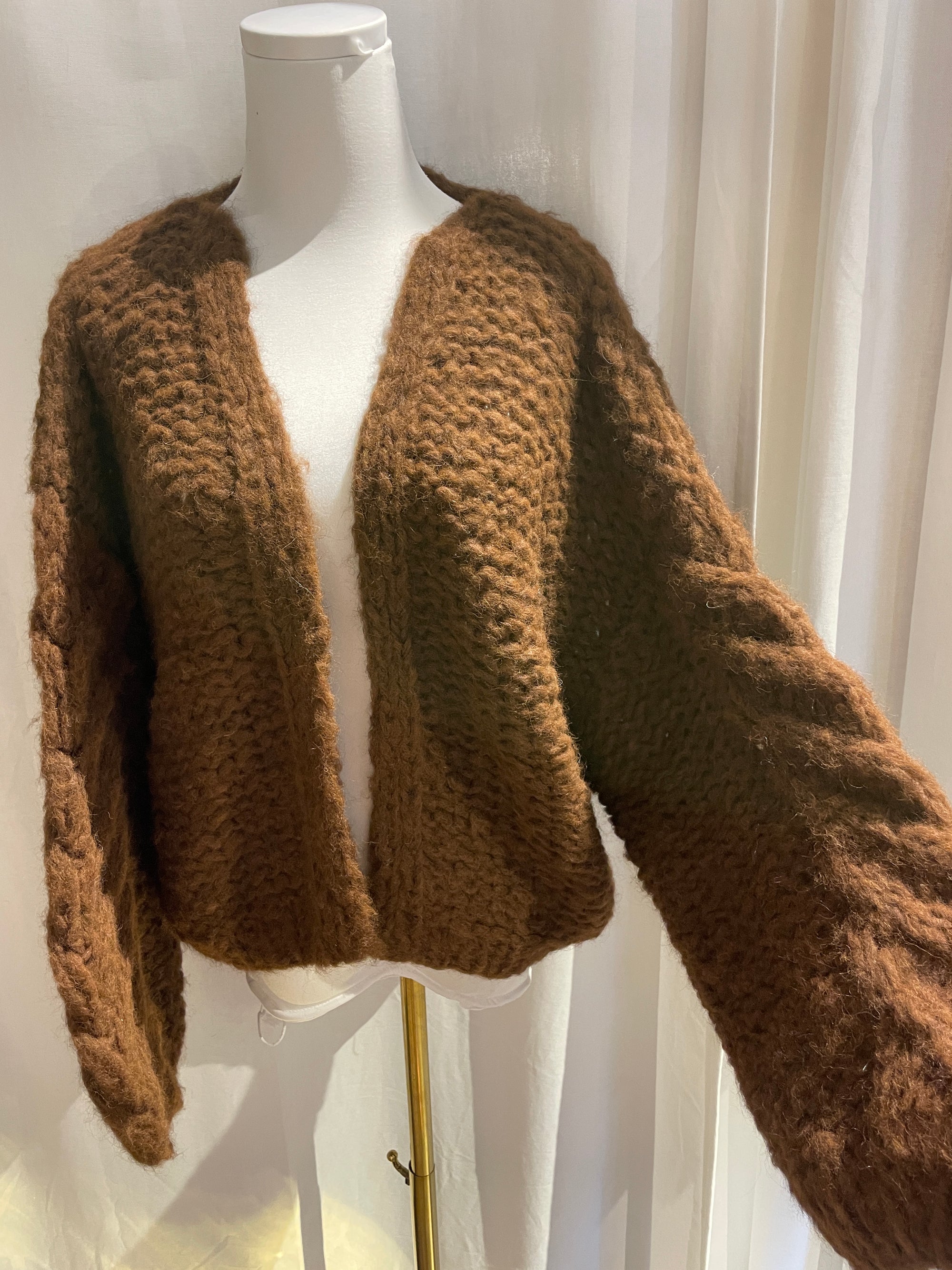 a white mannequin with a brown hand knit sweater hanging on it with a white background