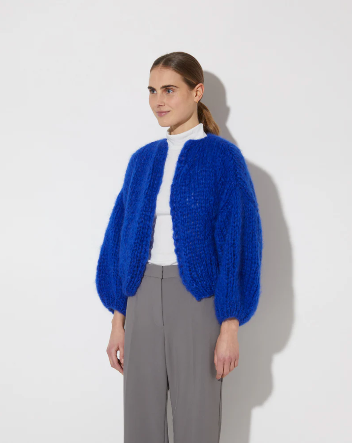 Person wearing a blue knitted cardigan over a white shirt on a light gray background