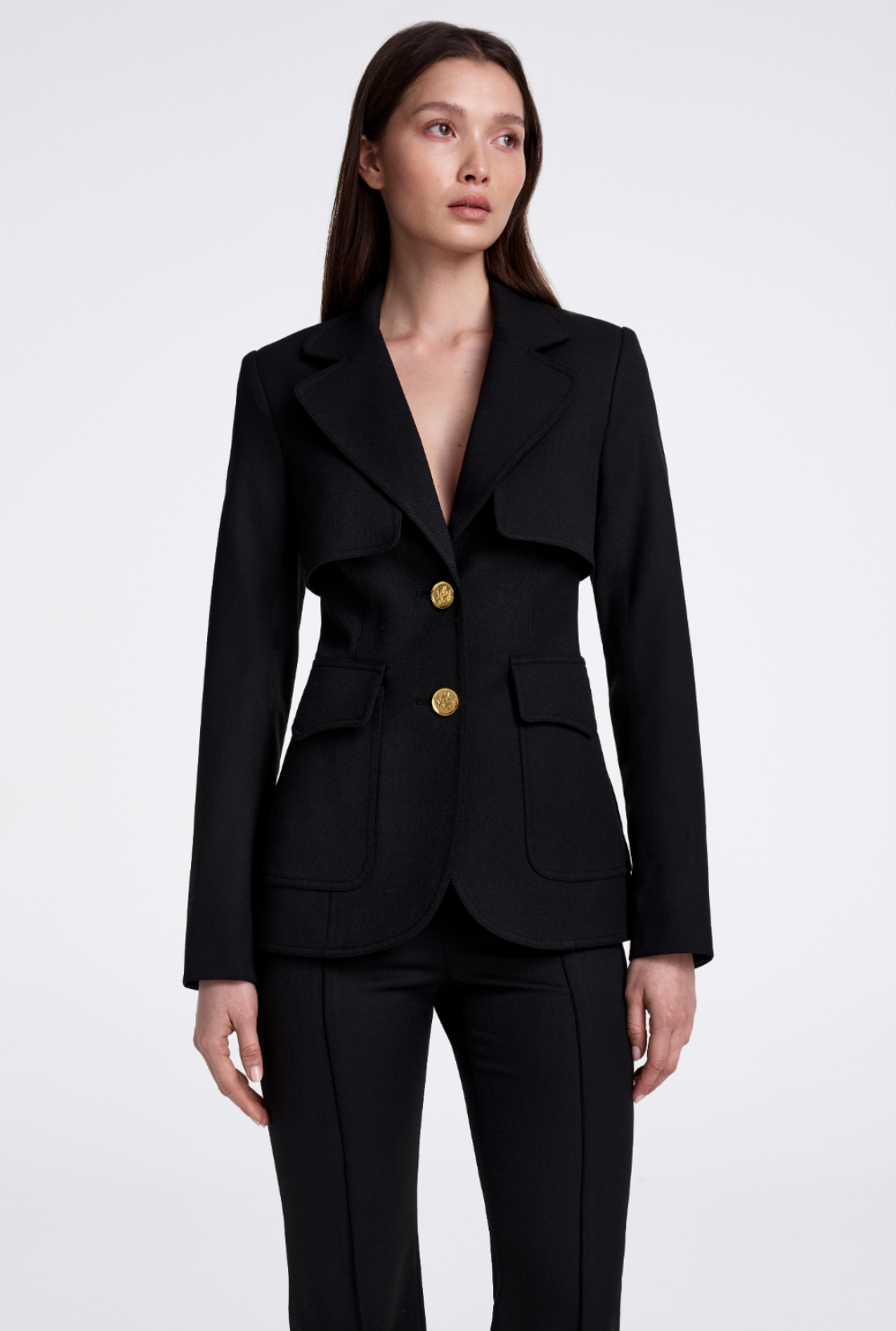 Woman wearing a black blazer with gold buttons on a white background