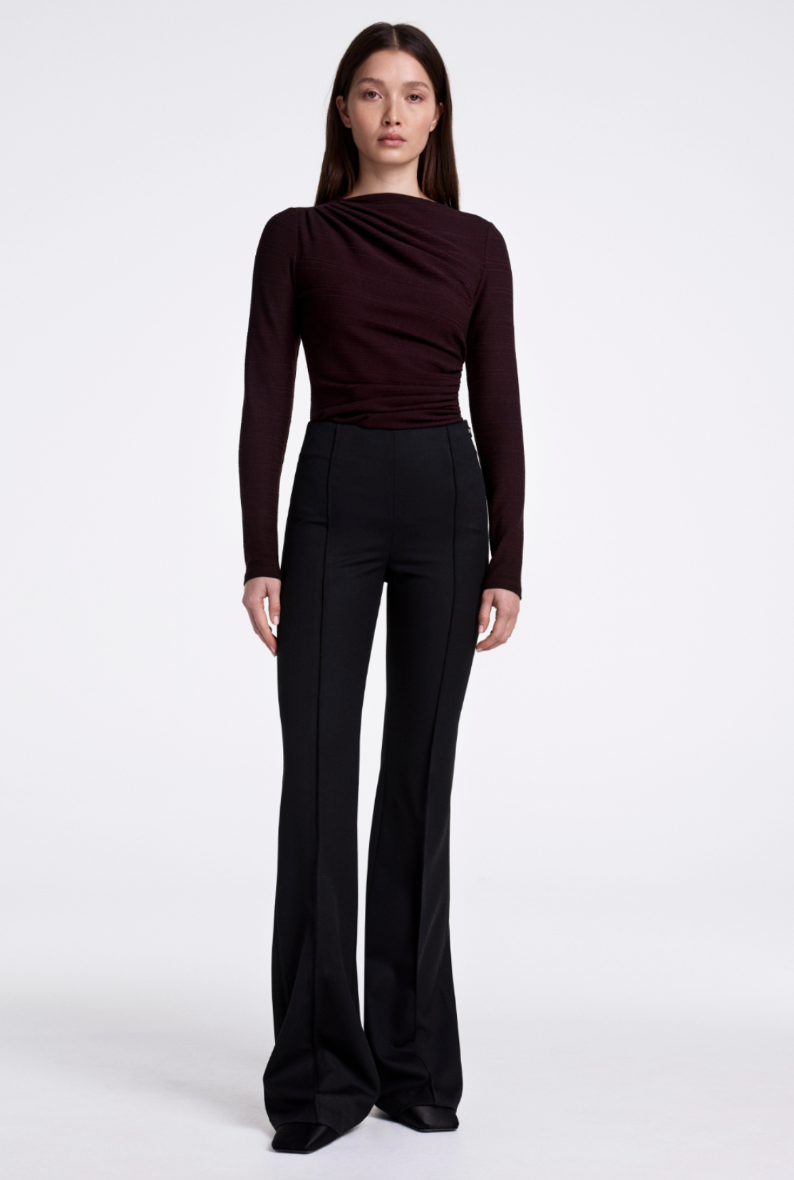Woman wearing a brown long-sleeve top and black pants on a white background