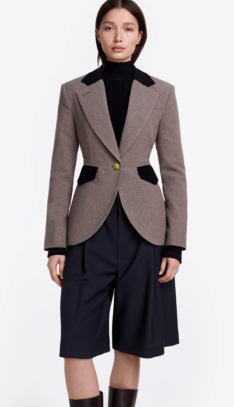 Woman wearing a brown blazer with black accents and navy skirt on a white background