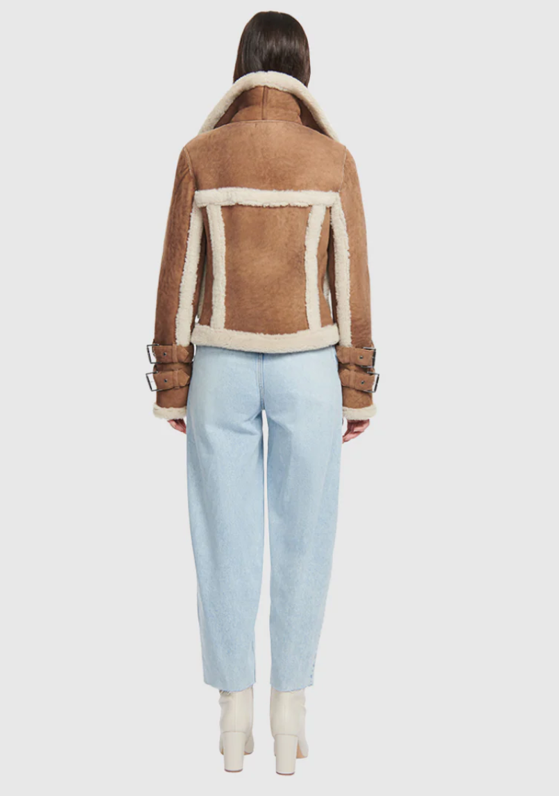 Person wearing a brown shearling jacket with white trim on a white background