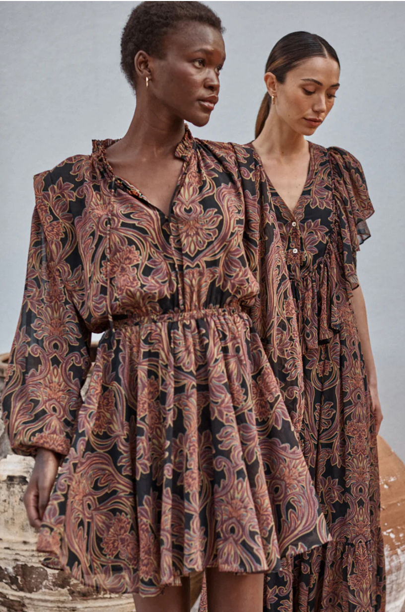 Two women wearing patterned dresses standing against a neutral background