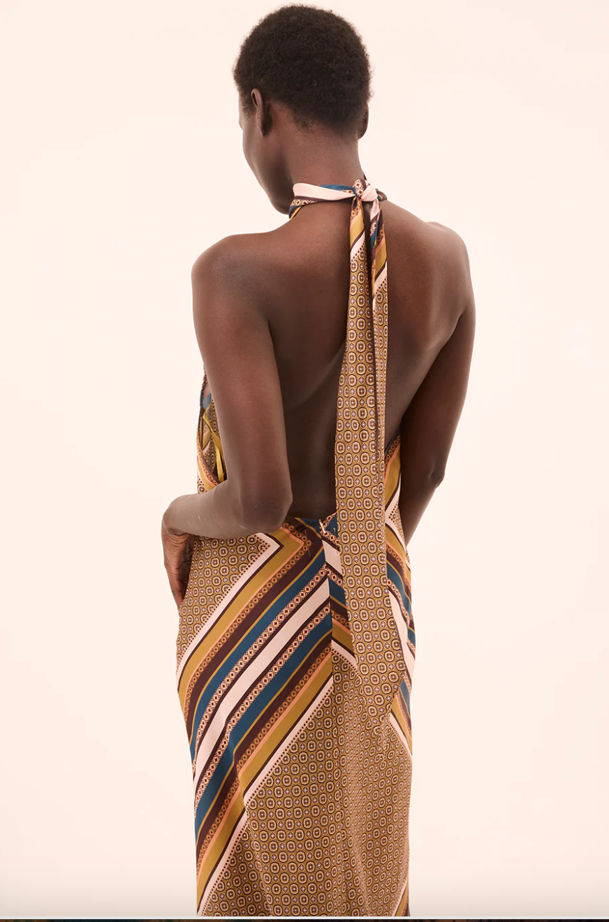 Woman wearing a patterned dress with a long scarf over her shoulder on a beige background