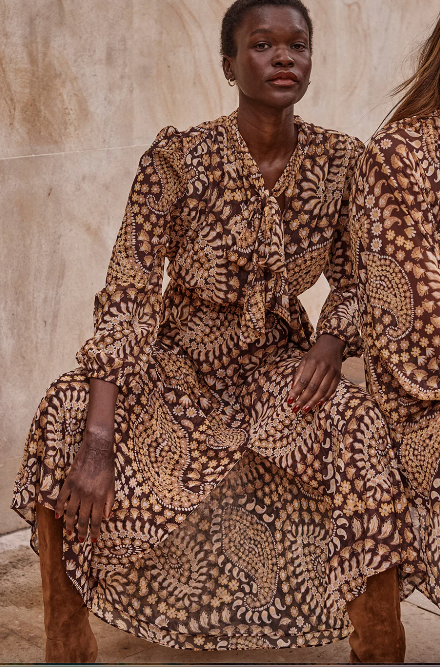 Woman wearing a patterned dress sitting against a neutral background