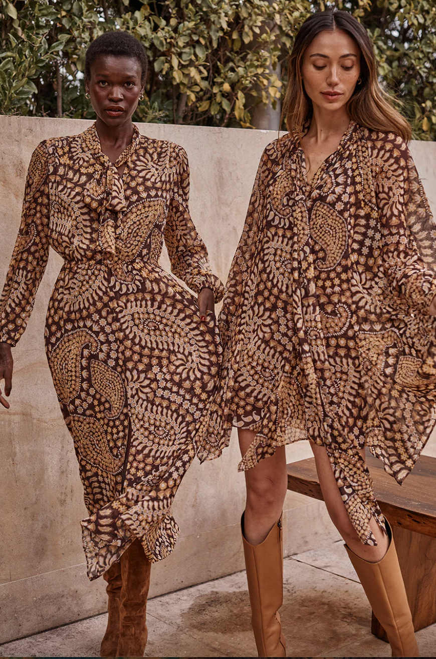 Two women wearing patterned outfits sitting on a stone bench outdoors.