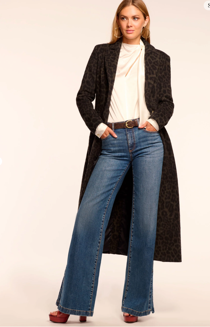 Woman wearing a long black coat, white top, and blue jeans on a plain background