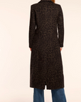 Person wearing a long black coat with a leopard print pattern on a beige background