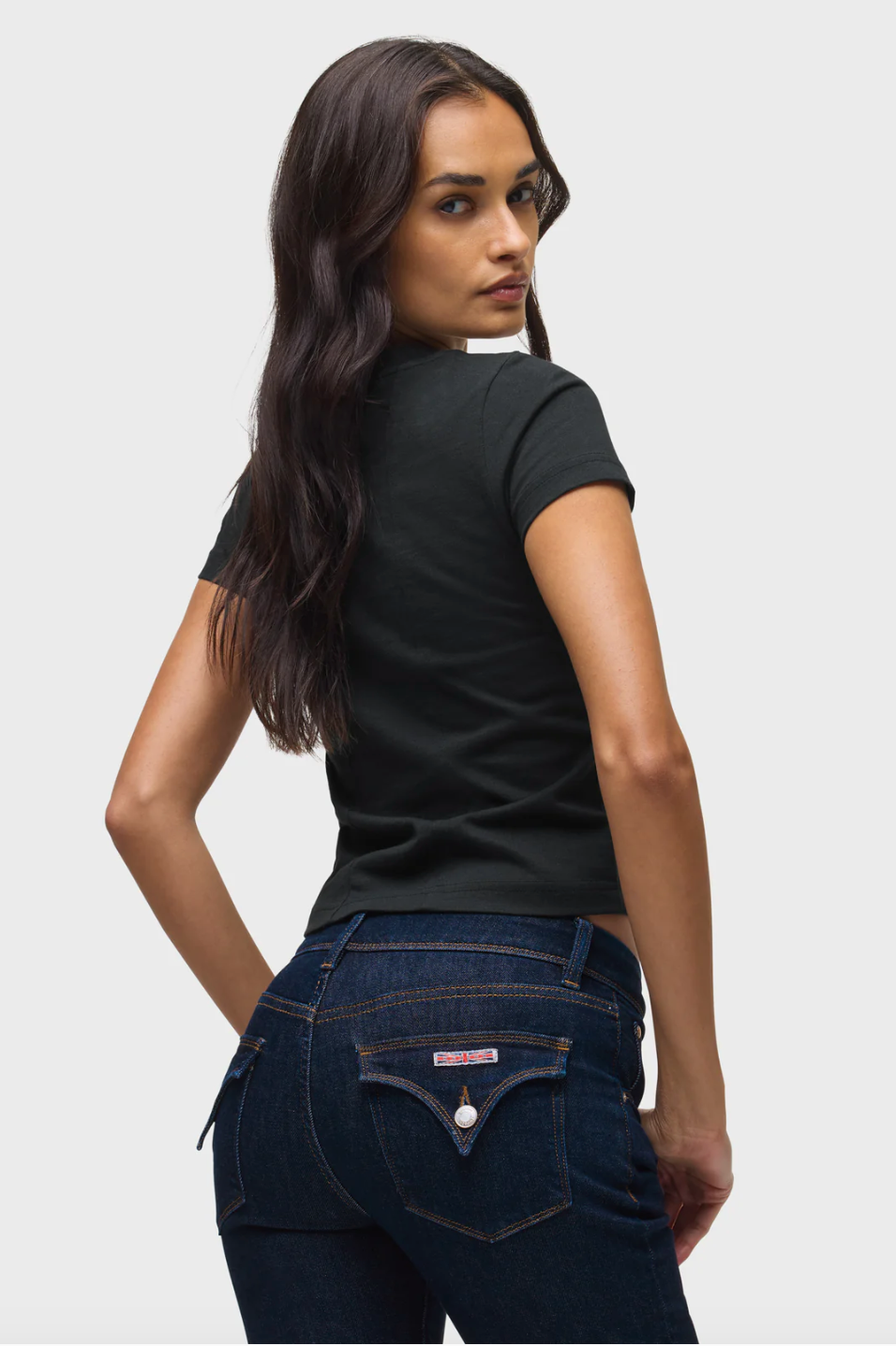 Woman wearing a black t-shirt and dark blue jeans on a light gray background