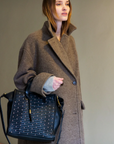 Woman in a brown coat holding a black handbag against a plain background
