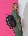 Woman holding a black backpack against a pink and white background