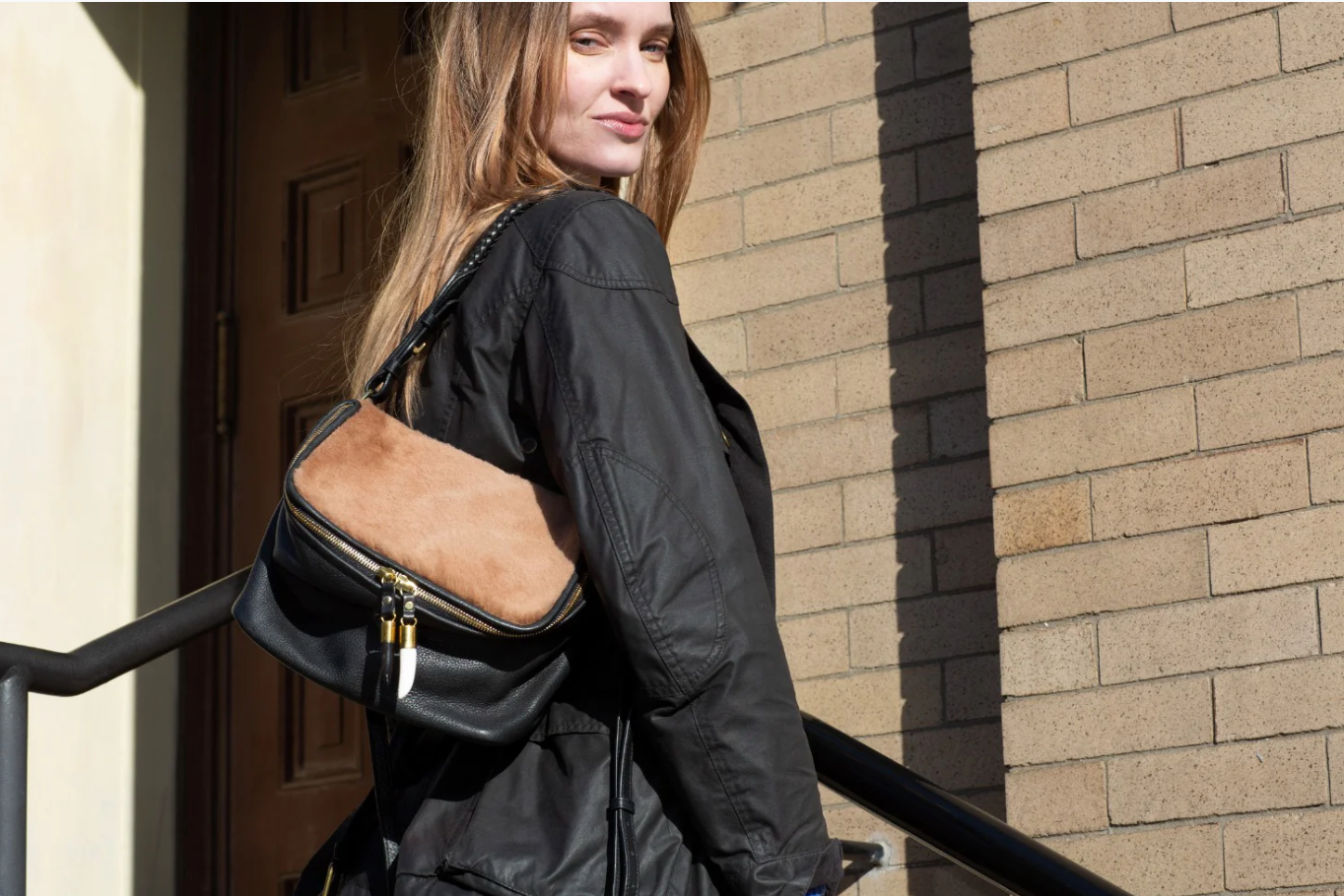 Woman carrying a black backpack with a brown patch on a brick building background
