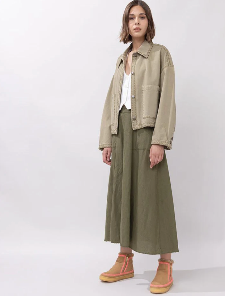 Person wearing a beige jacket and green pants on a white background