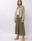 Person wearing a beige jacket and green pants on a white background