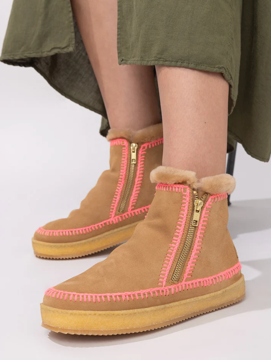 Tan winter boots with pink zippers worn by a person in an olive green skirt.
