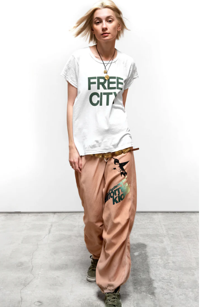 Person wearing a white 'Free City' t-shirt and beige pants on a plain background