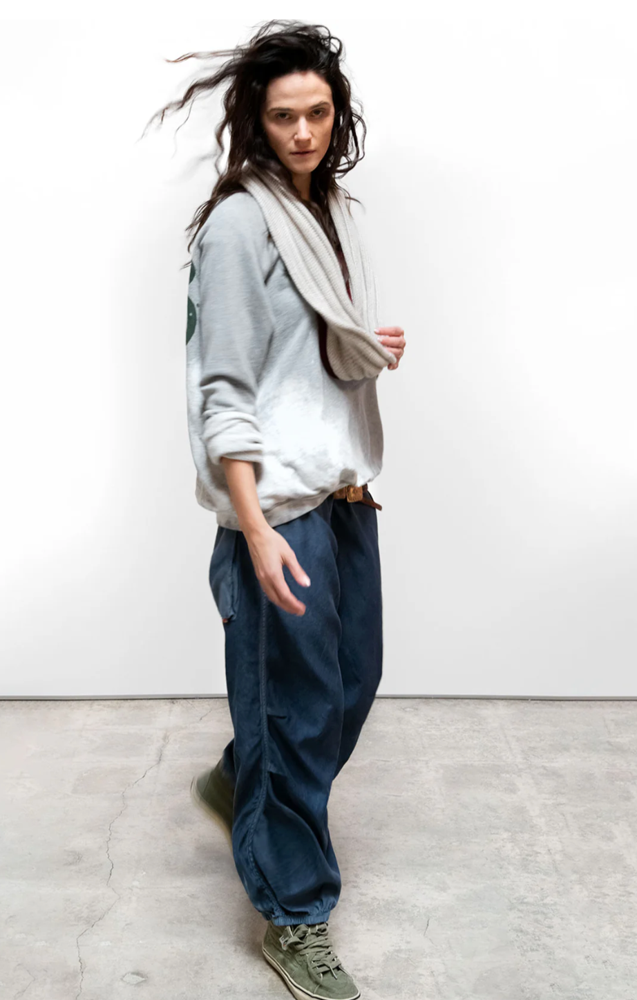 Woman wearing a gray sweater, beige scarf, and blue pants on a white background