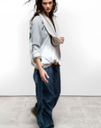 Woman wearing a gray sweater, beige scarf, and blue pants on a white background