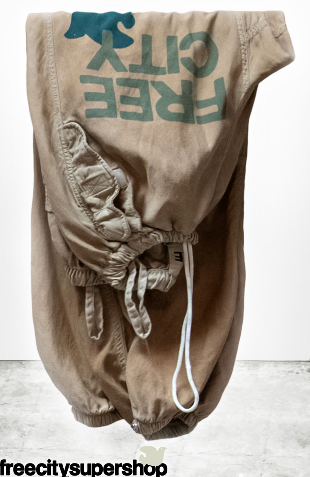 Beige baggy pants with 'Free City' text on a white background