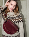 Woman wearing a patterned sweater with a maroon handbag against a decorative wall.