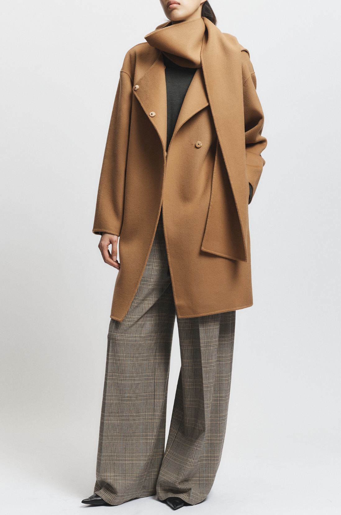 Person wearing a tan coat and plaid pants on a white background