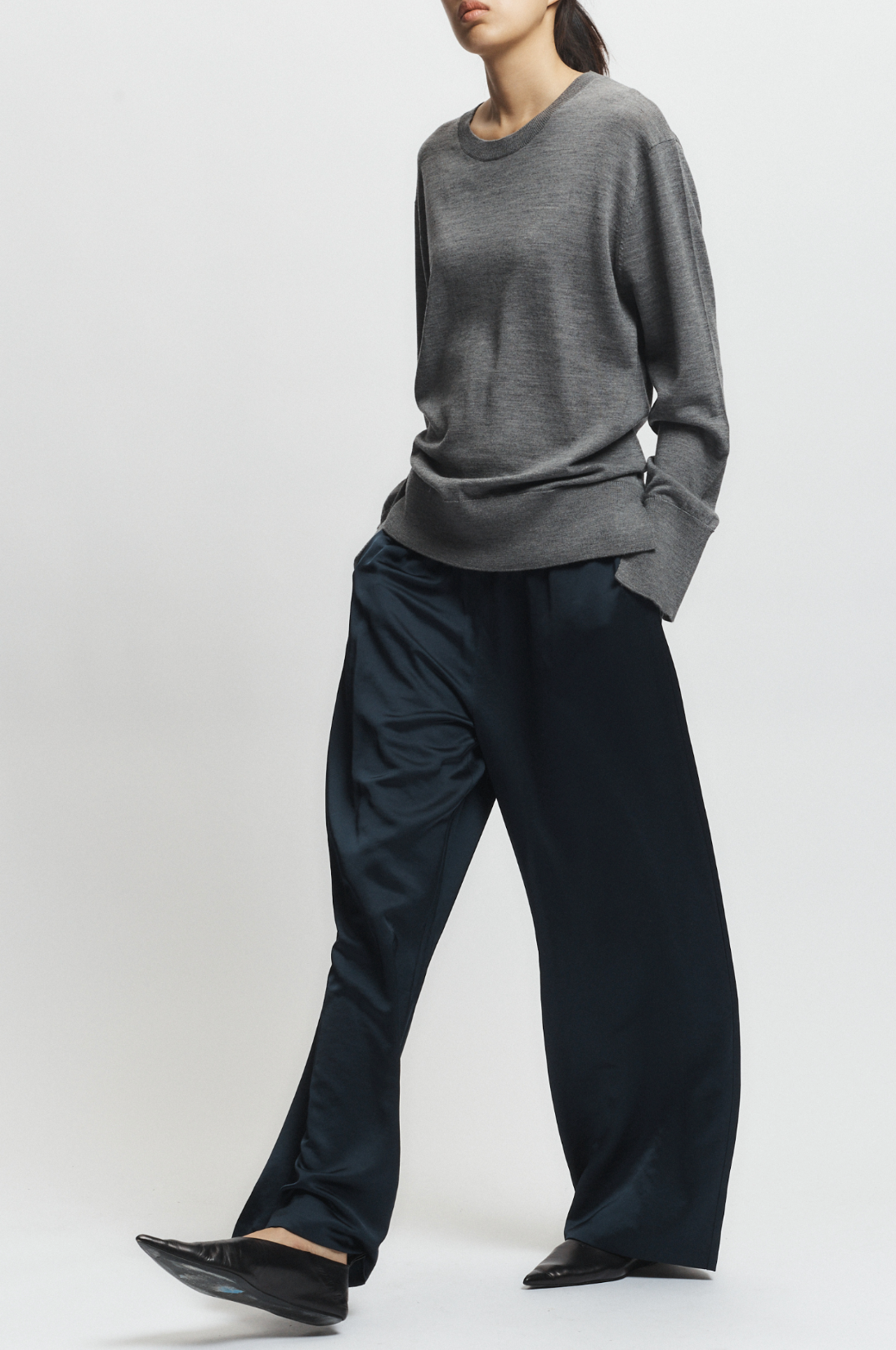 Person wearing a gray sweater and black pants on a white background