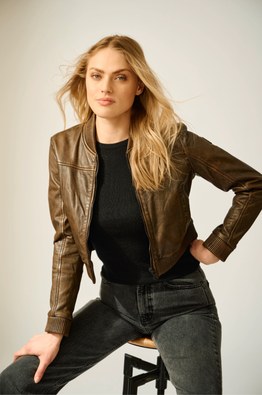 Woman wearing a brown leather jacket and black top against a plain background