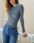 Woman wearing a gray sweater and blue jeans standing on a balcony.